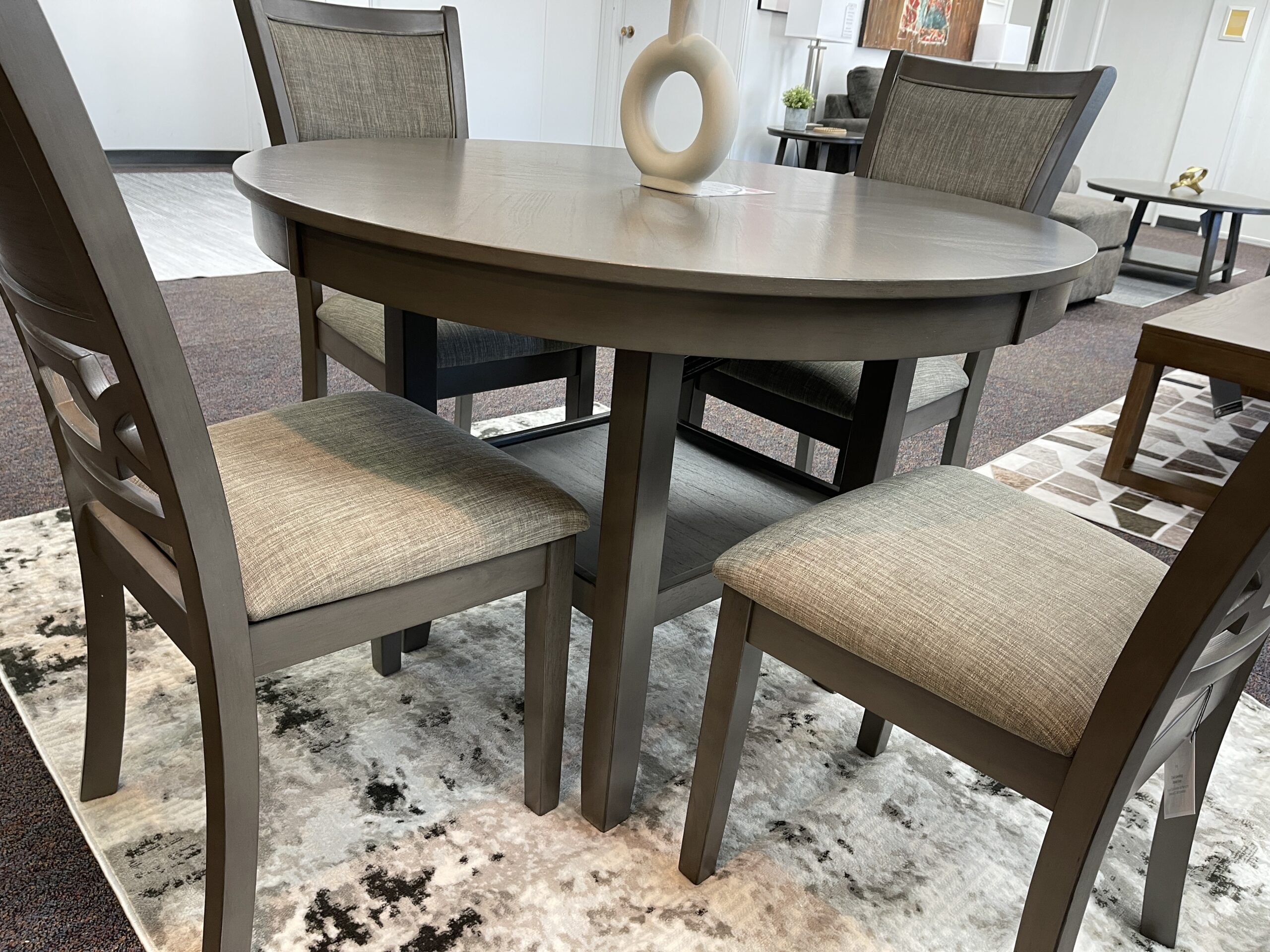 An Ashley Furniture Wrenning dining set featuring a transitional design in a modern light gray finish. The table showcases a reverse diamond patterned veneer top and thick tapered legs, paired with chairs that have decorative fretwork backrests and light gray textured upholstery, displayed at Forward Furniture Edmonton.