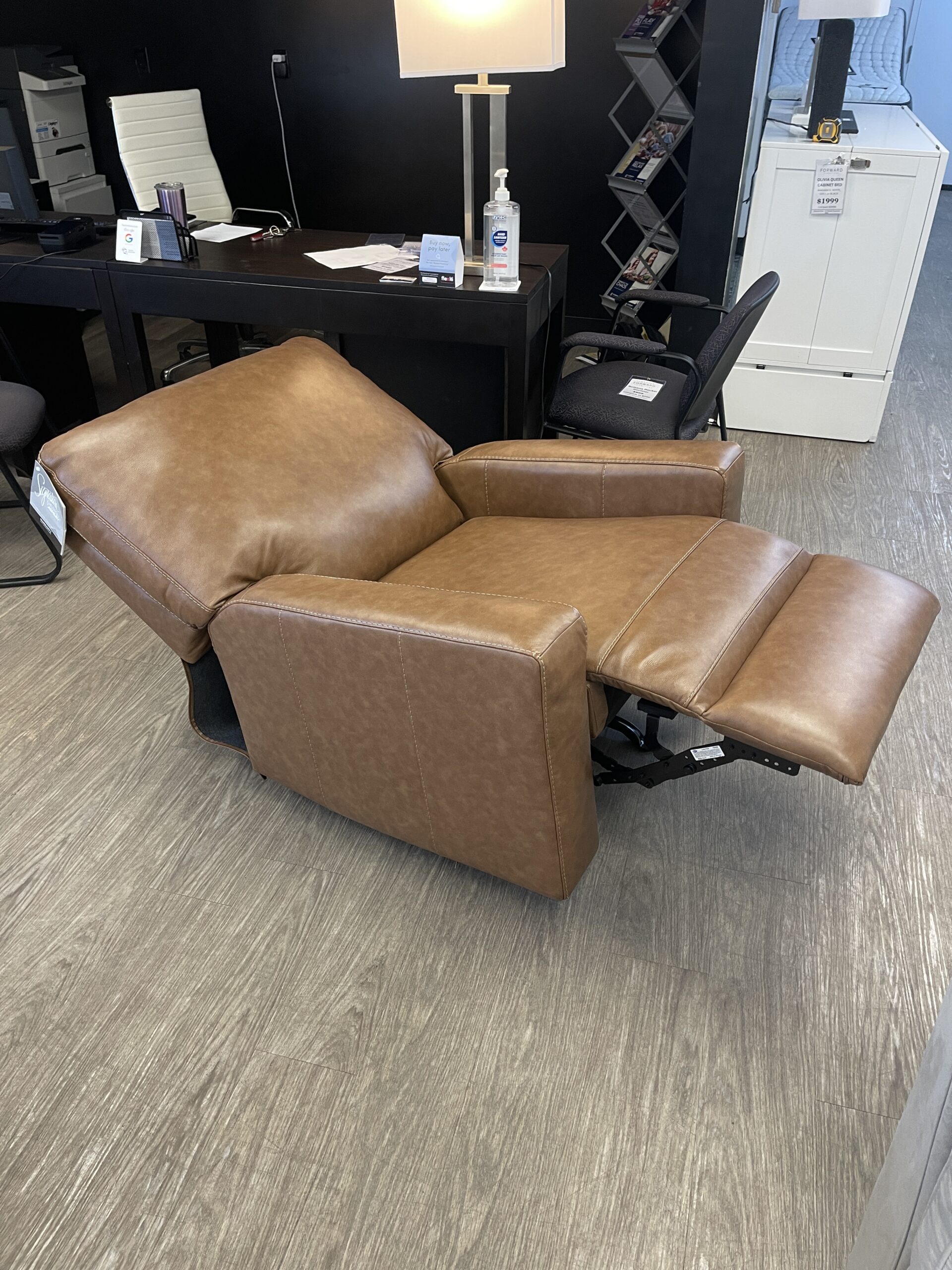 An Ashley Furniture Bolsena rocker recliner in a caramel leather, featuring a plush bustle back, thick padded armrests, and a manual reclining pull cord,, displayed at Forward Furniture Edmonton.