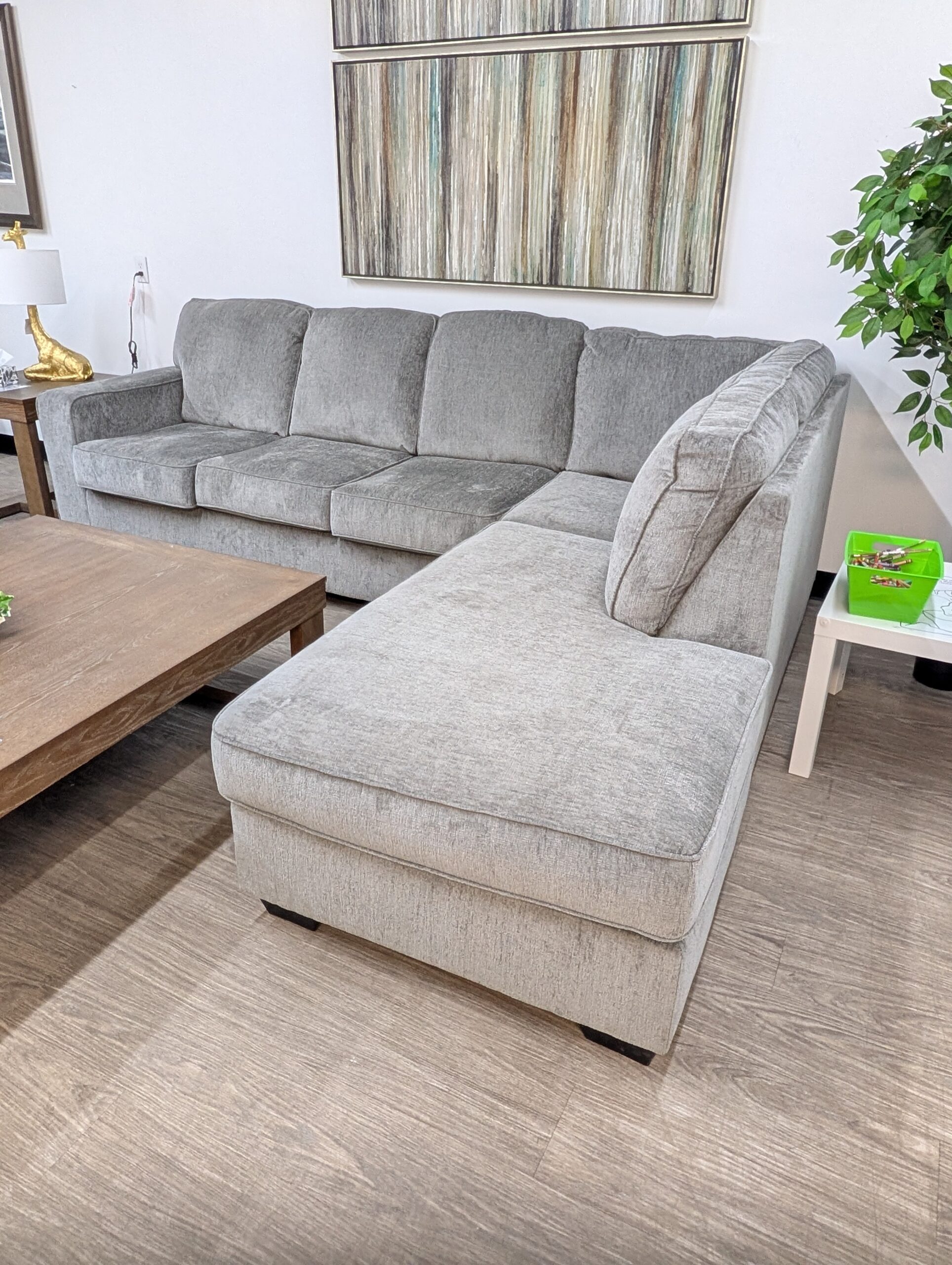 An Ashley Furniture Altari sectional sofa in light grey chenille fabric. It features sleek track arms, plush boxed cushions, and patterned accent pillows, displayed at the Forward Furniture Edmonton showroom.