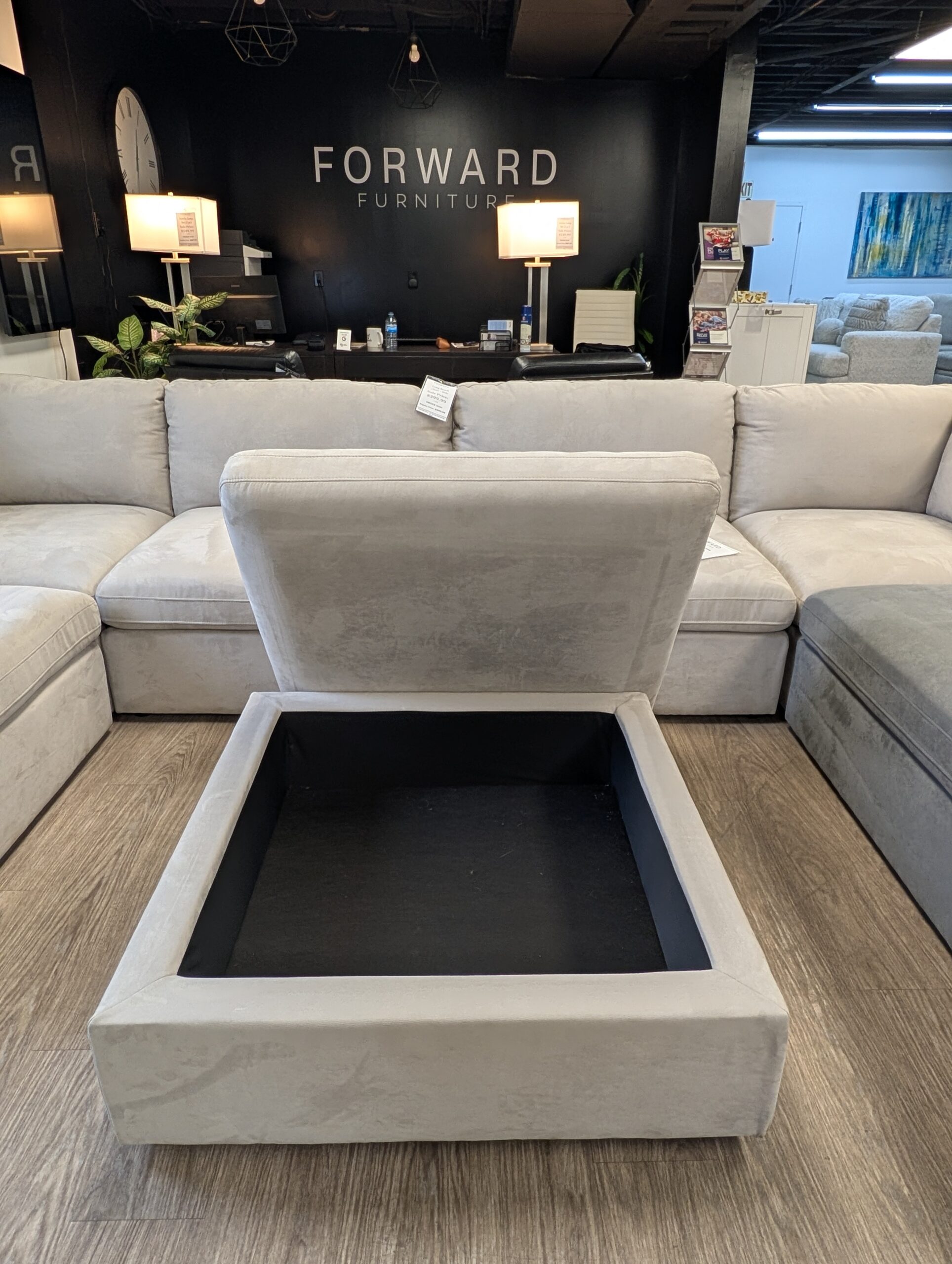 Open light grey Long Beach modular storage ottoman in front of a matching sectional at Forward Furniture