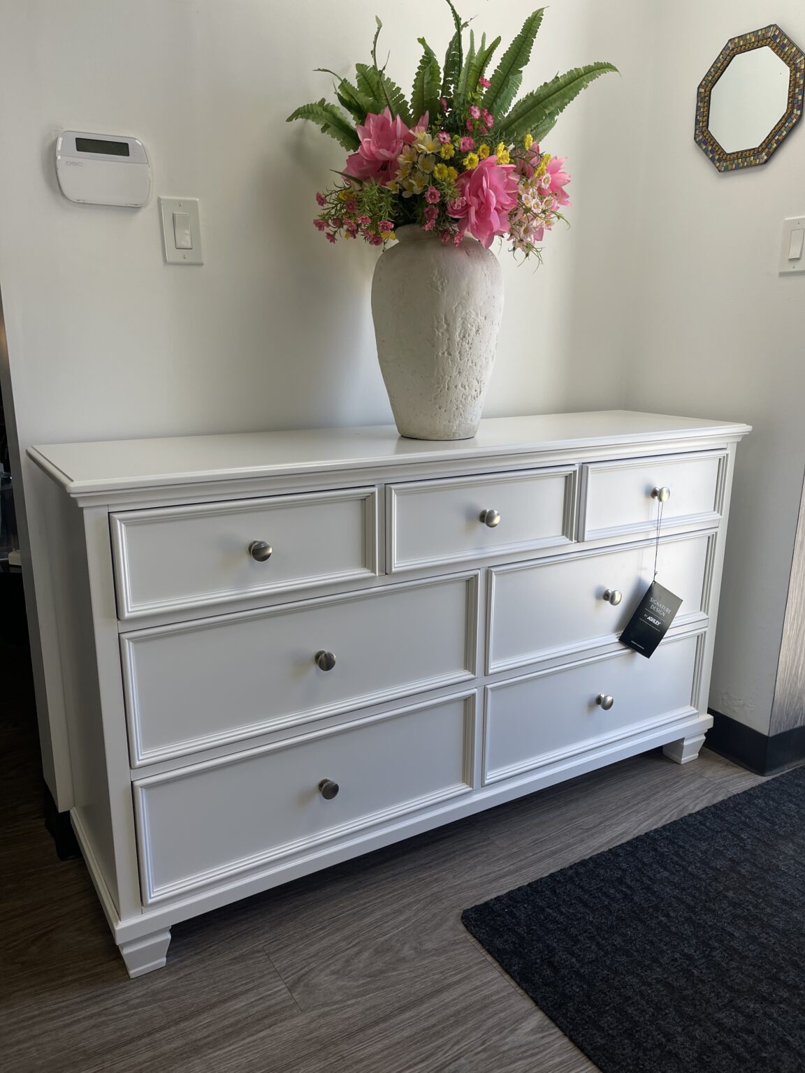 A modern white Ashley Fortman 7-drawer bureau featuring framed drawer fronts, satin nickel-tone round metal knobs, and tapered feet.